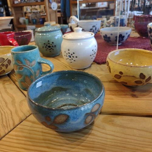 A variety of colorful ceramic bowls and mugs displayed on a wooden table.