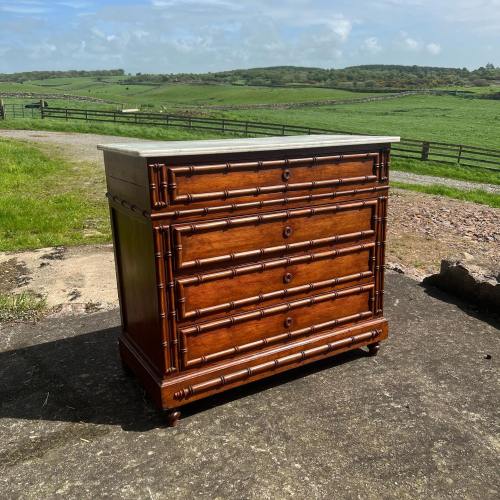 A wooden chest of drawers with a marble top, set against a scenic countryside backdrop.