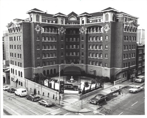 Historic hotel building with a central fountain, surrounded by palm trees and vintage cars parked on the street.