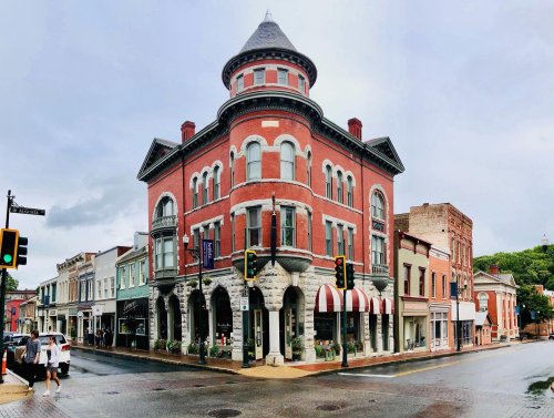 Historic red brick building at a street corner, featuring a turret and awnings, with shops lining the street.