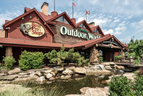 Exterior of Bass Pro Shops Outdoor World, featuring a rustic design, water features, and flags flying above.
