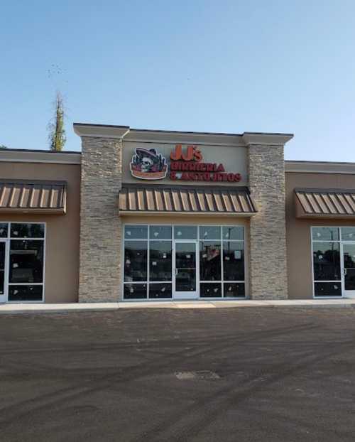 Exterior of a restaurant with a stone facade and large windows, featuring the sign "Jus Burritos & Tacos."