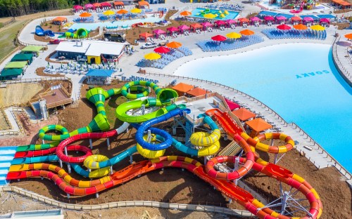 Aerial view of a vibrant water park featuring colorful slides, a large pool, and numerous lounge areas.