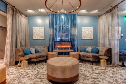 Cozy lounge area with plush seating, a modern fireplace, and decorative curtains against a blue wall.