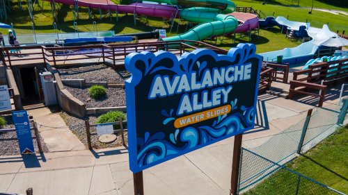 Sign for "Avalanche Alley Water Slides" with colorful water slides in the background and a grassy area.