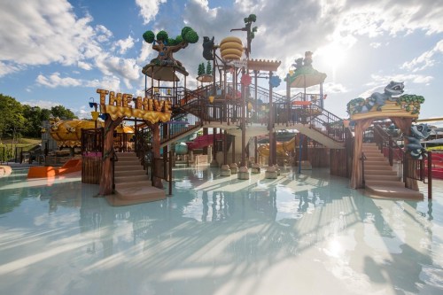 A colorful water park play area with slides, stairs, and themed decorations under a bright sky.