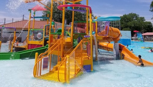 Colorful water slides and play structures in a sunny pool area, with children enjoying the water.