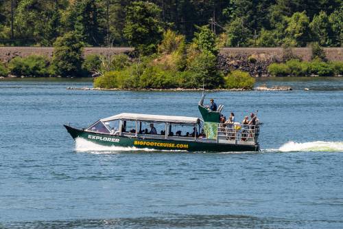 A tour boat named "Explorer" with passengers cruising on a river surrounded by trees and greenery.