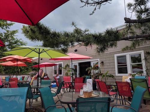 Outdoor dining area with colorful umbrellas, tables, and chairs, surrounded by greenery and a cloudy sky.