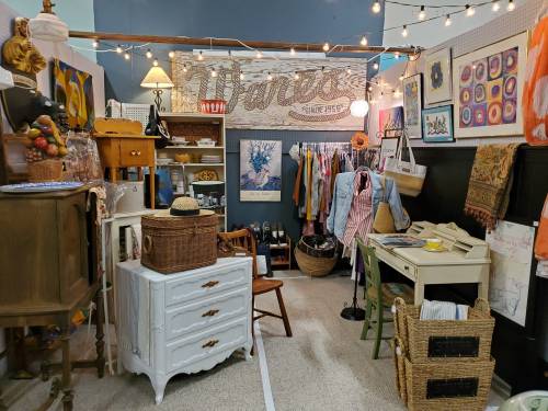 A cozy vintage shop filled with clothing, decor, and furniture, illuminated by string lights.