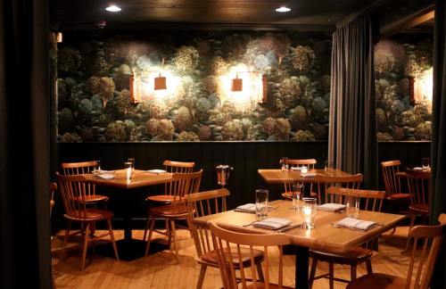 Cozy restaurant interior with wooden tables, chairs, and a decorative wall featuring a floral pattern. Soft lighting enhances ambiance.