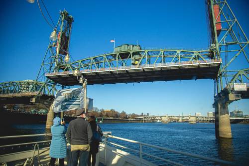 A group of people on a boat watches a bridge lift over a river on a clear day.