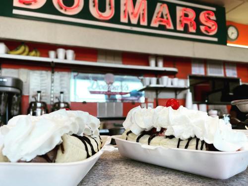 Two banana splits topped with whipped cream and cherries, with a retro diner sign in the background.