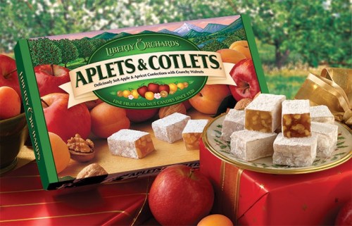 A box of Applets & Cotlets candy with pieces displayed, surrounded by apples and walnuts on a festive background.