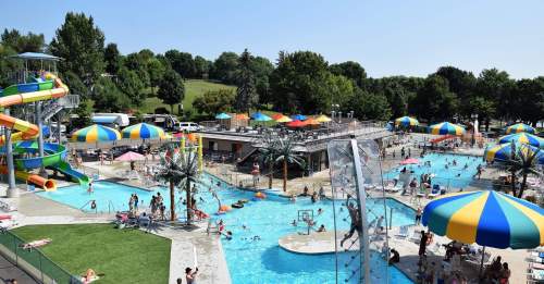 A vibrant outdoor pool area with water slides, colorful umbrellas, and people enjoying the sun and water activities.