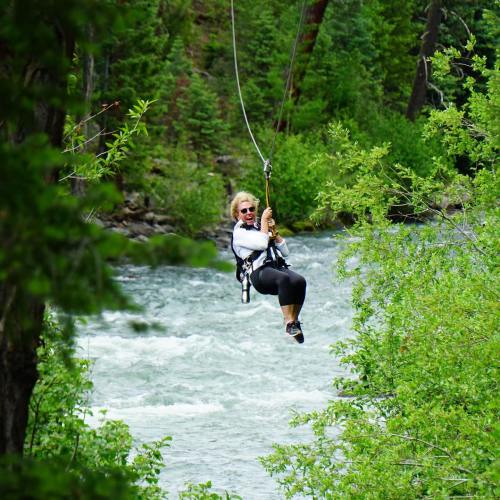 A woman zip-lining over a river, surrounded by lush green trees and a scenic landscape.