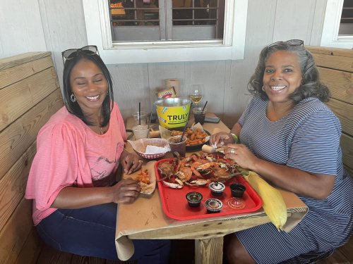 Two women enjoying a seafood meal at a restaurant, smiling with a spread of food on the table.