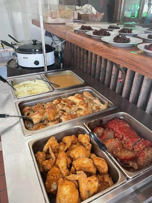 A buffet display featuring fried chicken, mashed potatoes, gravy, and various meat dishes on a wooden counter.