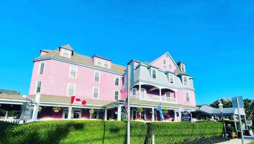 A large pink hotel with gray accents under a clear blue sky, surrounded by greenery and outdoor seating.
