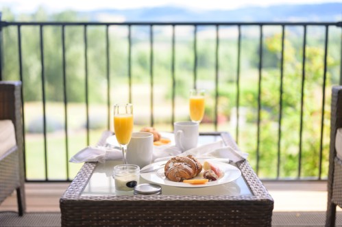 A cozy breakfast spread on a balcony table, featuring croissants, fruit, and drinks, with a scenic view in the background.