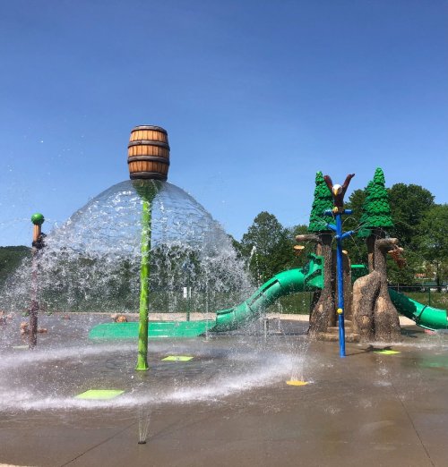A colorful splash pad with water features, including a large barrel and slides, set against a clear blue sky.