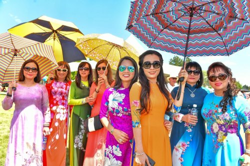 A group of women in colorful traditional dresses holding umbrellas, smiling together outdoors on a sunny day.