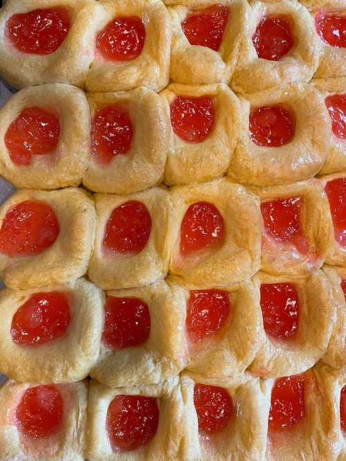A close-up of freshly baked sweet rolls with a glossy red fruit filling in the center of each roll.