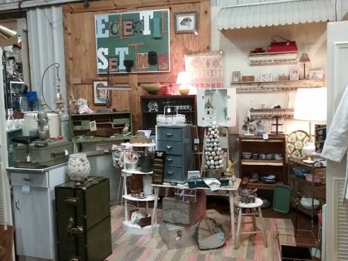 A cozy vintage shop display featuring various antiques, furniture, and decorative items arranged on wooden walls.