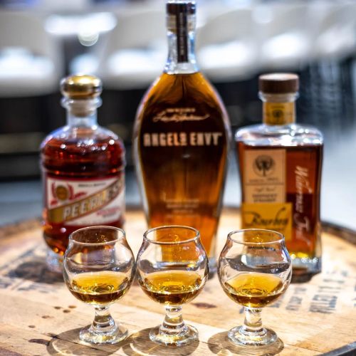 A selection of whiskey bottles with three tasting glasses filled with amber liquid on a wooden barrel.