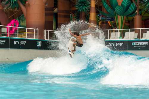 A young surfer performs a jump on a wave in an indoor surf park, surrounded by tropical decor.