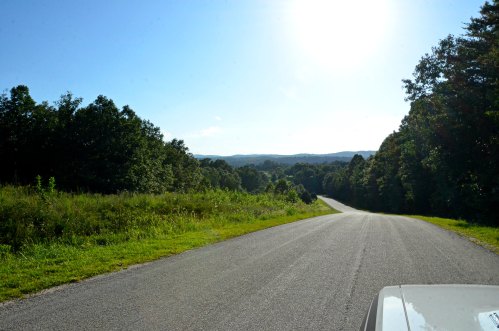 A winding road stretches through lush greenery under a clear blue sky, with mountains in the distance.