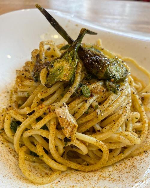 A plate of spaghetti topped with green vegetables and spices, served in a white dish.