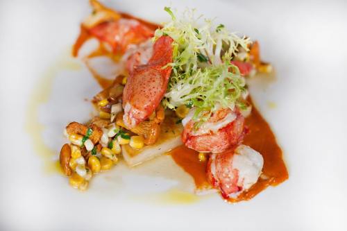 A gourmet dish featuring lobster, corn, and greens drizzled with sauce on a white plate.