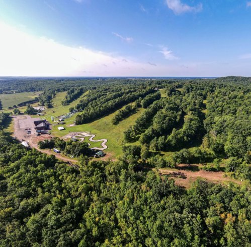 Aerial view of lush green hills and a small building surrounded by trees under a clear blue sky.