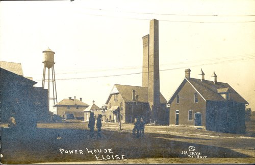Historic photo of the Eloise Power House, featuring buildings and a water tower, with people in the foreground.