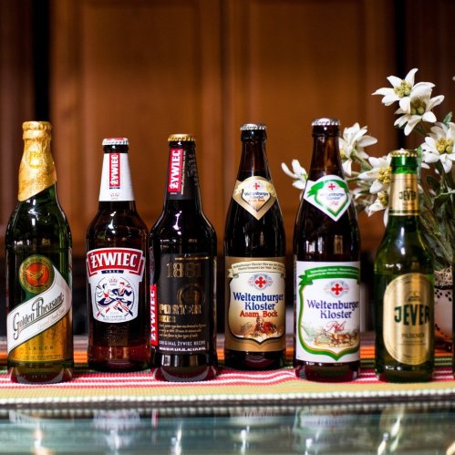 A variety of beer bottles displayed on a table, with a floral centerpiece in the background.