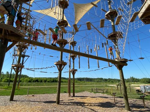 A high ropes course with various climbing structures and participants navigating the obstacles against a clear blue sky.