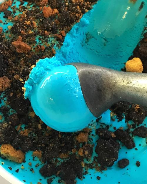 A close-up of a blue ice cream scoop on a bed of crushed cookies and crumbs.