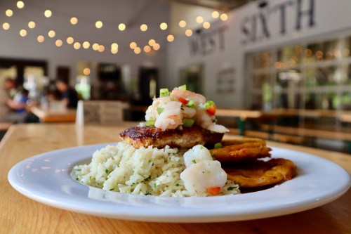 A plate of grilled fish topped with shrimp salsa, served on a bed of rice with fried plantains, in a cozy restaurant setting.
