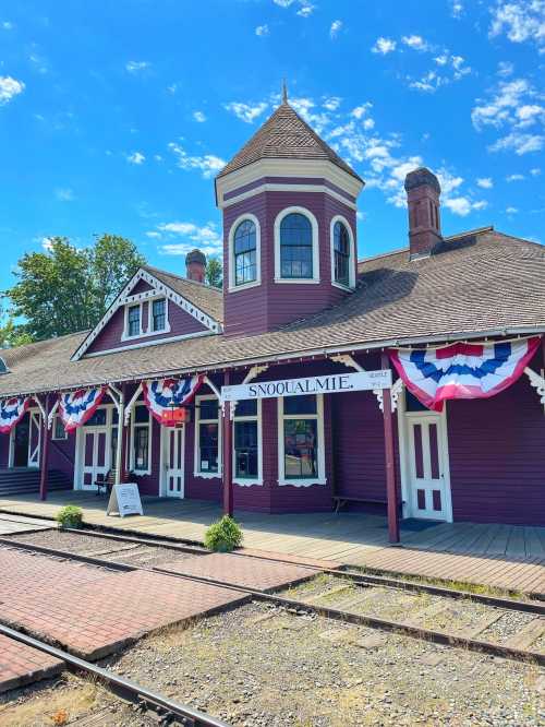 Historic Snoqualmie train station with red and white bunting, blue sky, and tracks in the foreground.