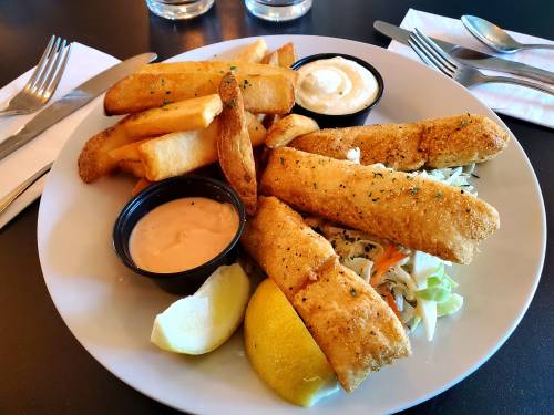A plate of golden fried fish fillets, coleslaw, lemon, and crispy fries with dipping sauces.