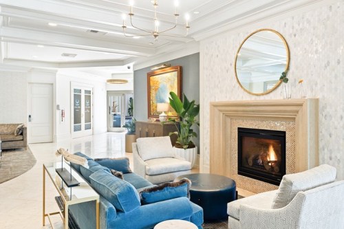 A stylish lobby with blue sofas, a round coffee table, a fireplace, and modern decor, featuring a large mirror and artwork.