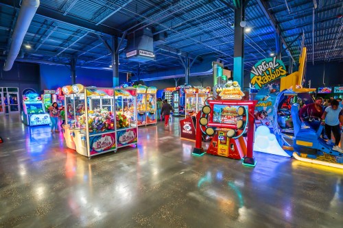 A vibrant arcade filled with various games and attractions, featuring colorful machines and visitors enjoying the space.