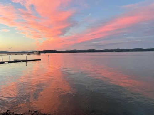 A serene lake at sunset, reflecting vibrant pink and orange clouds in the water, with distant hills in the background.
