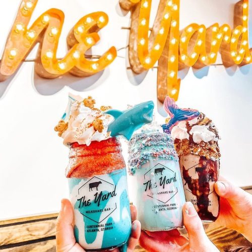 Three colorful milkshakes in jars topped with whipped cream and sprinkles, held in front of a "The Yard" sign.