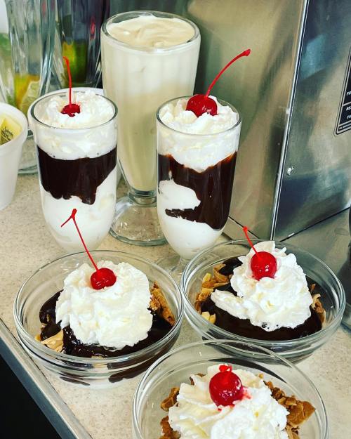 A variety of desserts featuring whipped cream, chocolate sauce, and cherries on top, served in bowls and glasses.