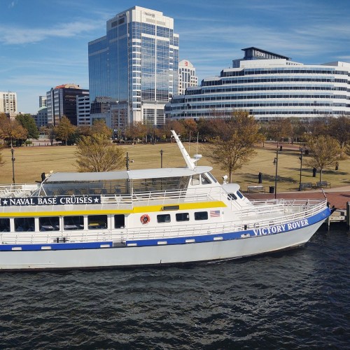 A boat named "Victory Rover" docked near modern buildings and green spaces along the waterfront.