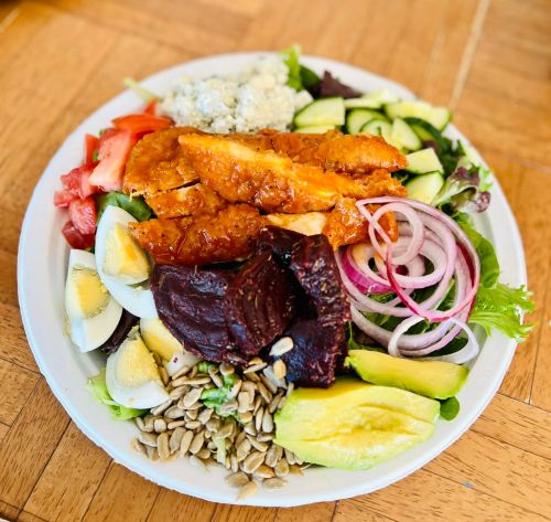 A colorful salad with fried chicken, boiled eggs, beets, avocado, cucumbers, tomatoes, and mixed greens on a plate.