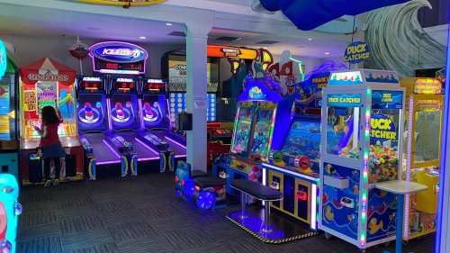 A vibrant arcade with various games, including skee-ball, a claw machine, and colorful lights.