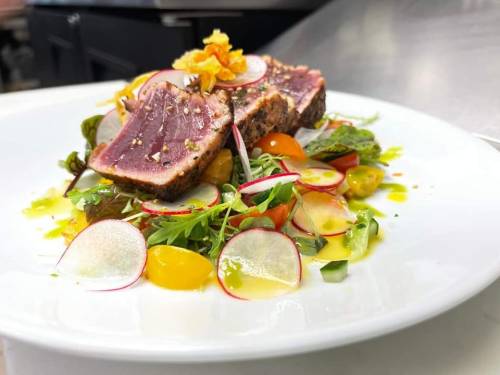 A beautifully plated dish featuring seared tuna on a bed of colorful salad with radishes and cherry tomatoes.